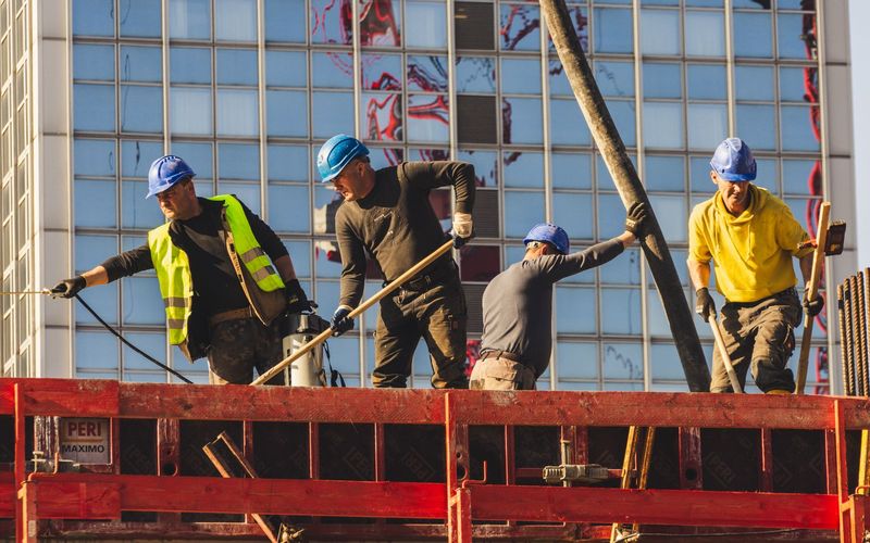 A group of construction workers in safety gear actively working on a high-rise building site